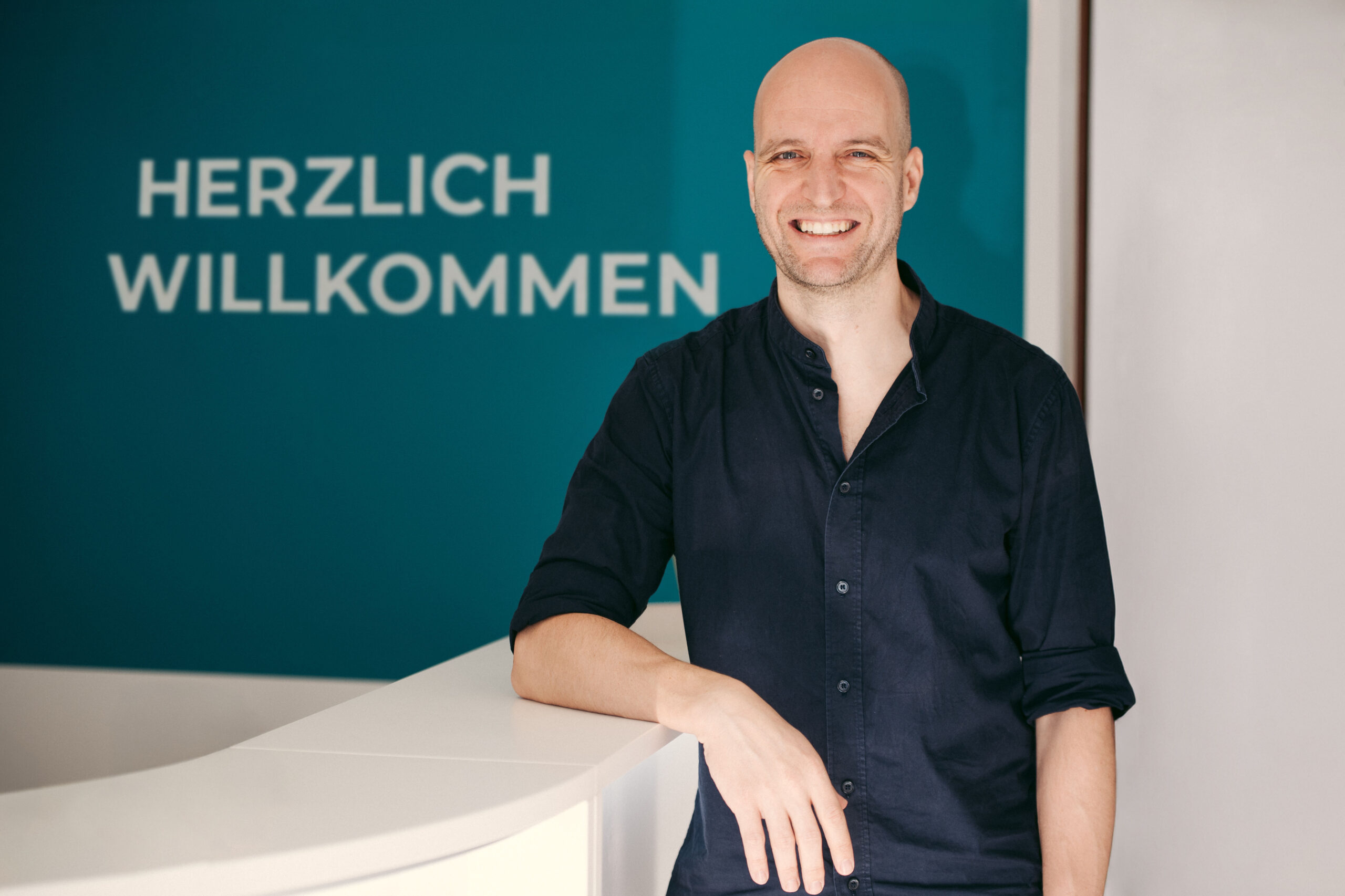 Philipp Gehrke lächelt am Empfang seiner Osteopathiepraxis in Alt-Hürth.